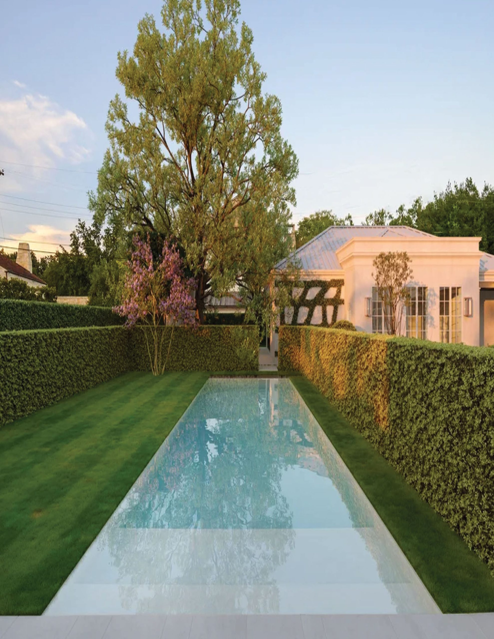 Park Cities – Crescent — Lap pool flanked by clipped hedges with pool house pavilion beyond at dusk