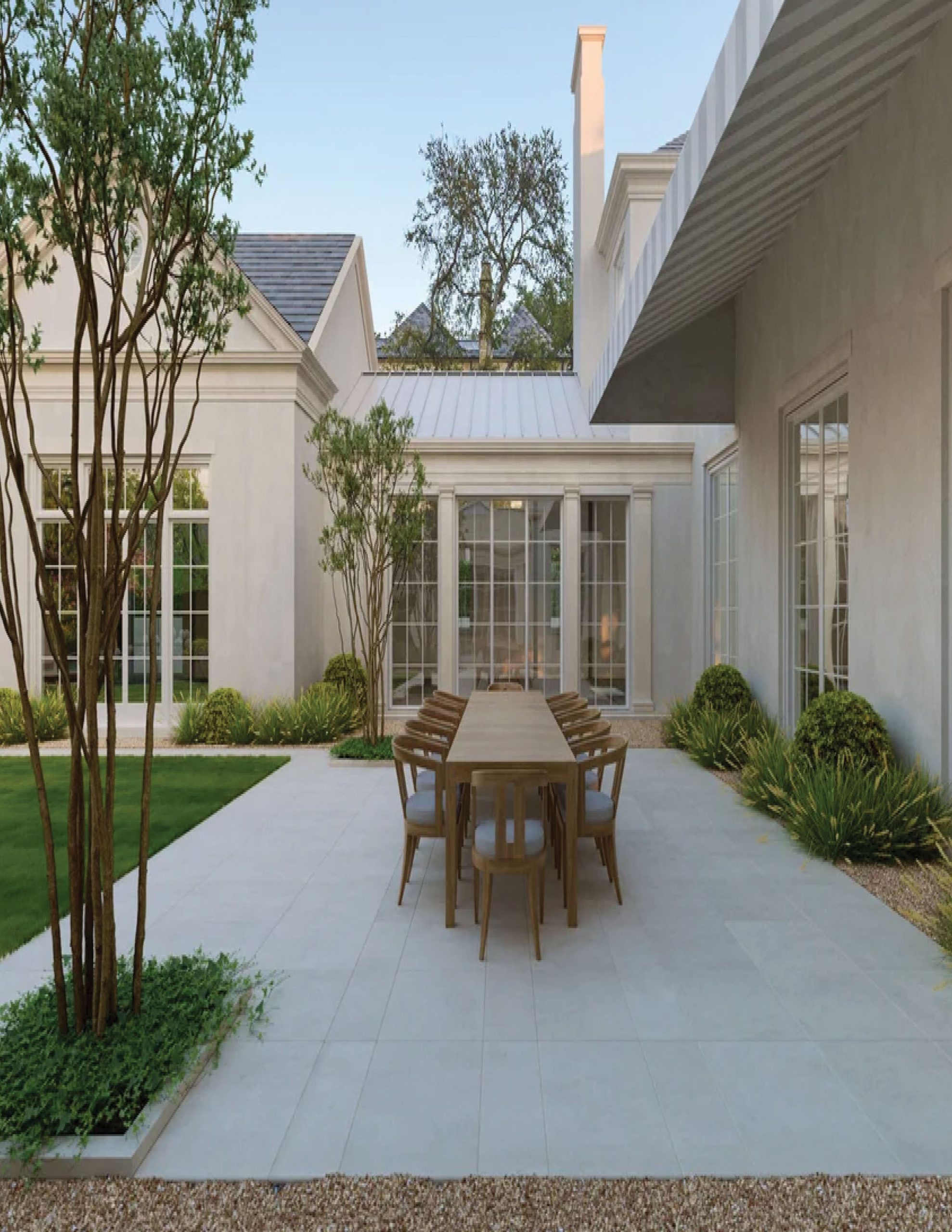 Park Cities – Crescent — Open-air courtyard with outdoor dining table and stone fireplace at dusk
