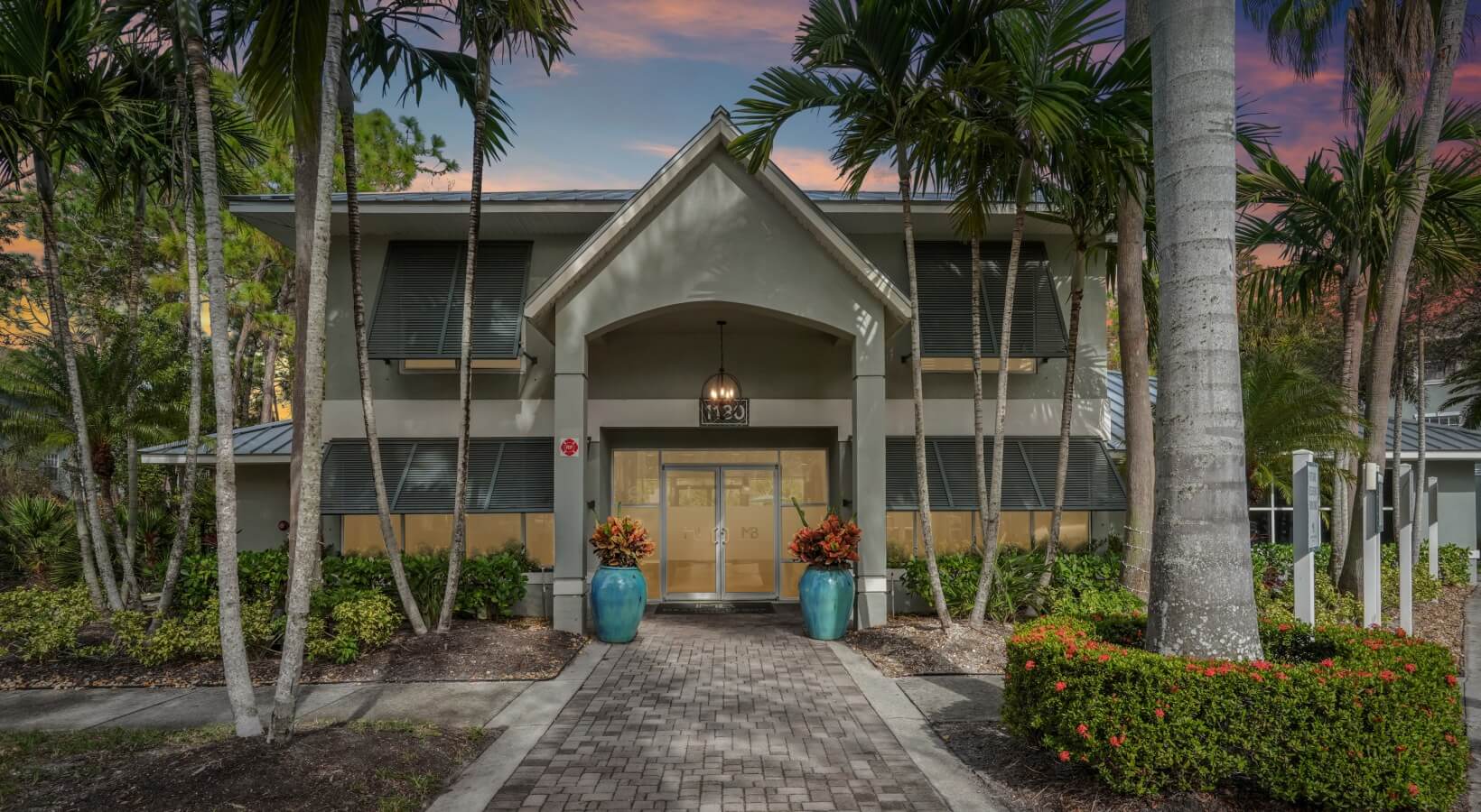 Meadow Brook Preserve — Clubhouse entrance at dusk with palm trees and landscape lighting
