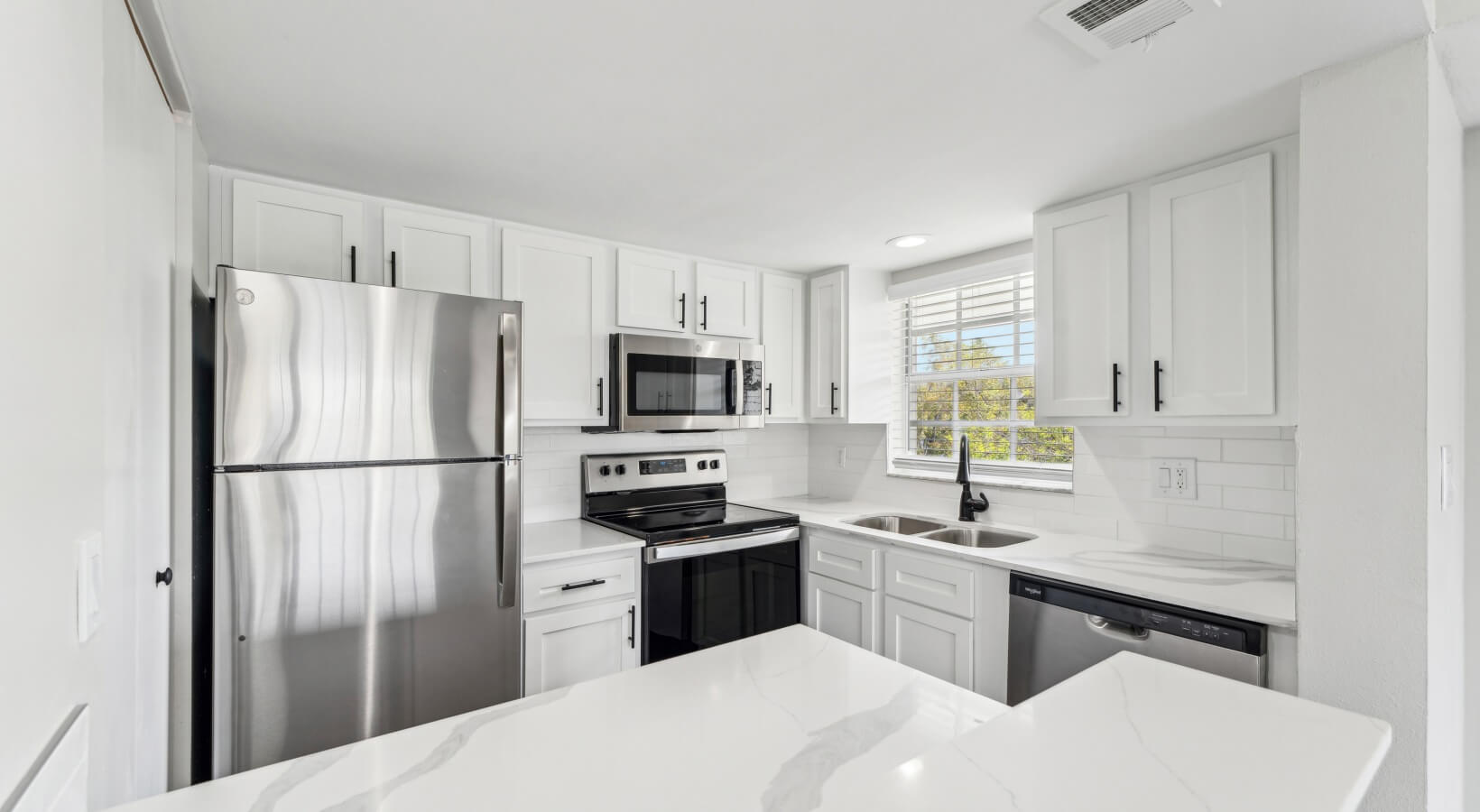 The Lennox — Renovated kitchen with white shaker cabinets, quartz countertops, and stainless appliances