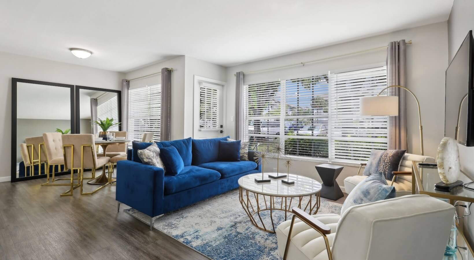 The Lennox — Renovated living room with blue velvet sofa, gold accent furnishings, and new flooring