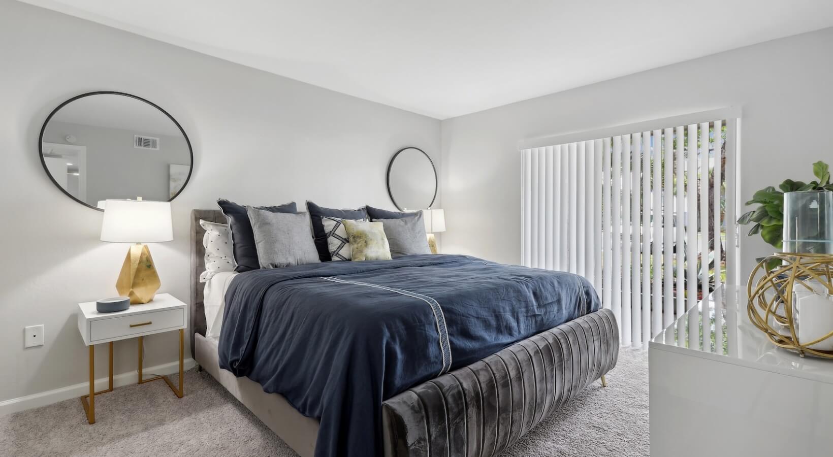 The Lennox — Renovated primary bedroom with new carpet, round mirrors, and gold accent lamps