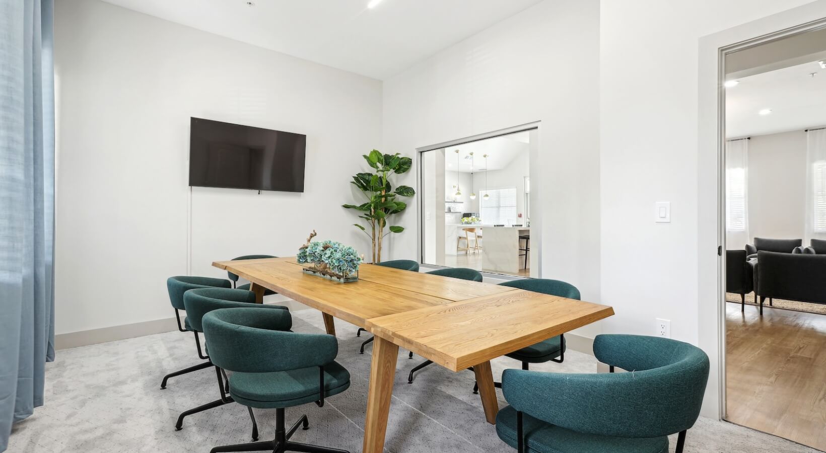 The Lennox — Renovated conference room with wood table, teal chairs, and adjacent resident lounge
